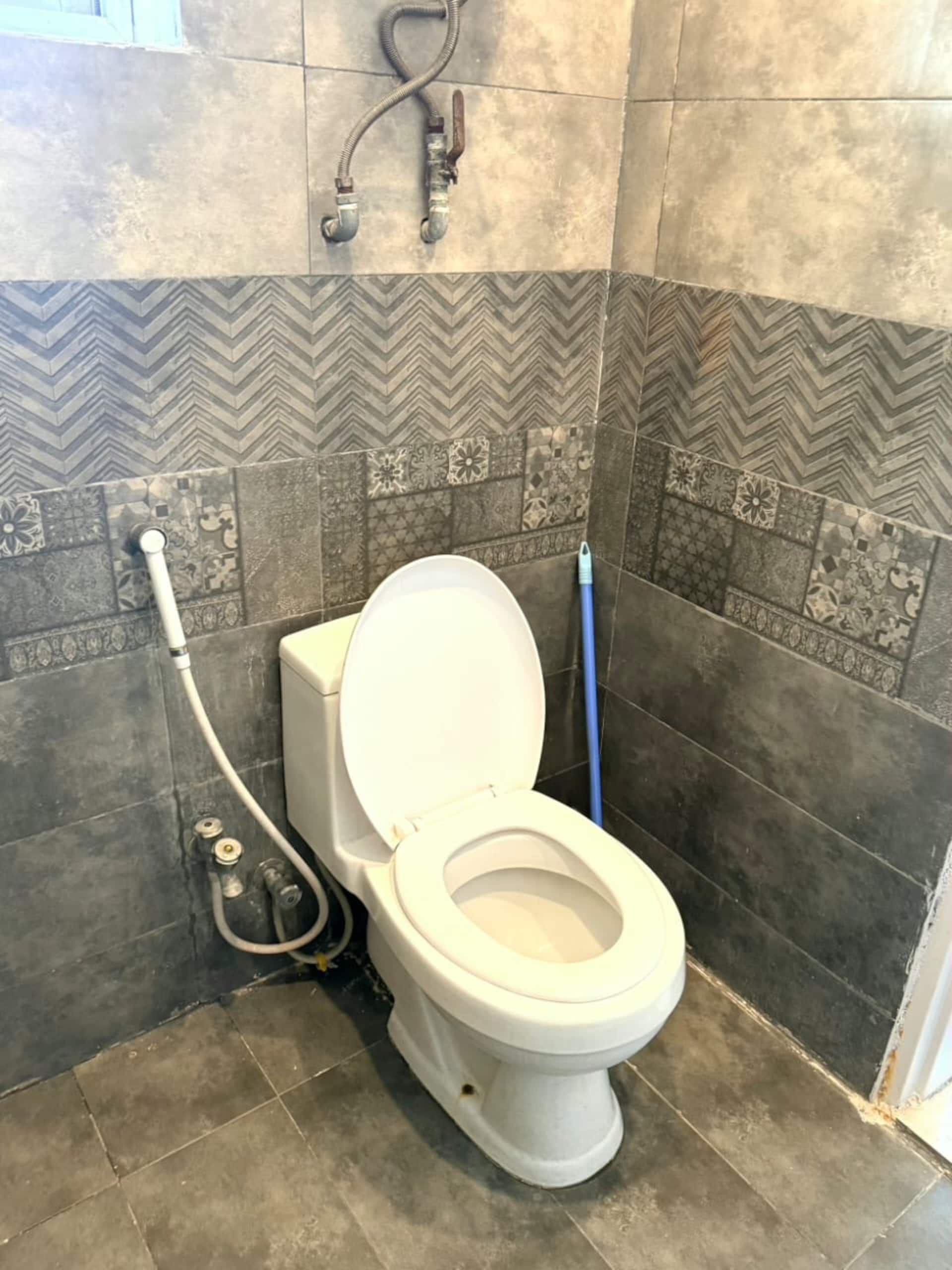 Tiled bathroom with WC and hand shower in The Amber Haven, the Aangan one-bedroom apartment facing Grand Jamia Mosque in Bahria Town Lahore