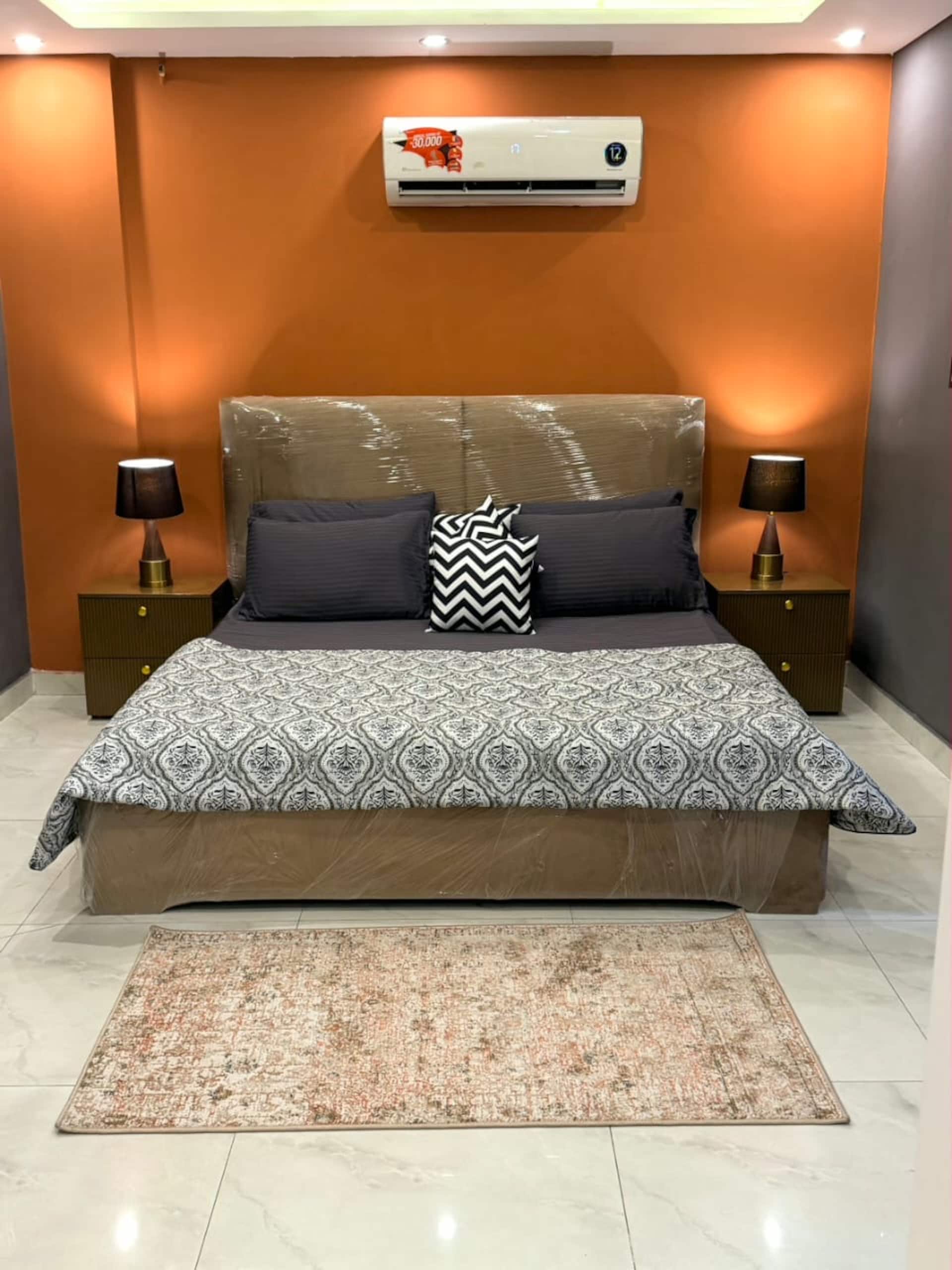 Bedroom with a king bed against a warm amber feature wall in The Amber Haven, the Aangan one-bedroom apartment facing Grand Jamia Mosque in Bahria Town Lahore