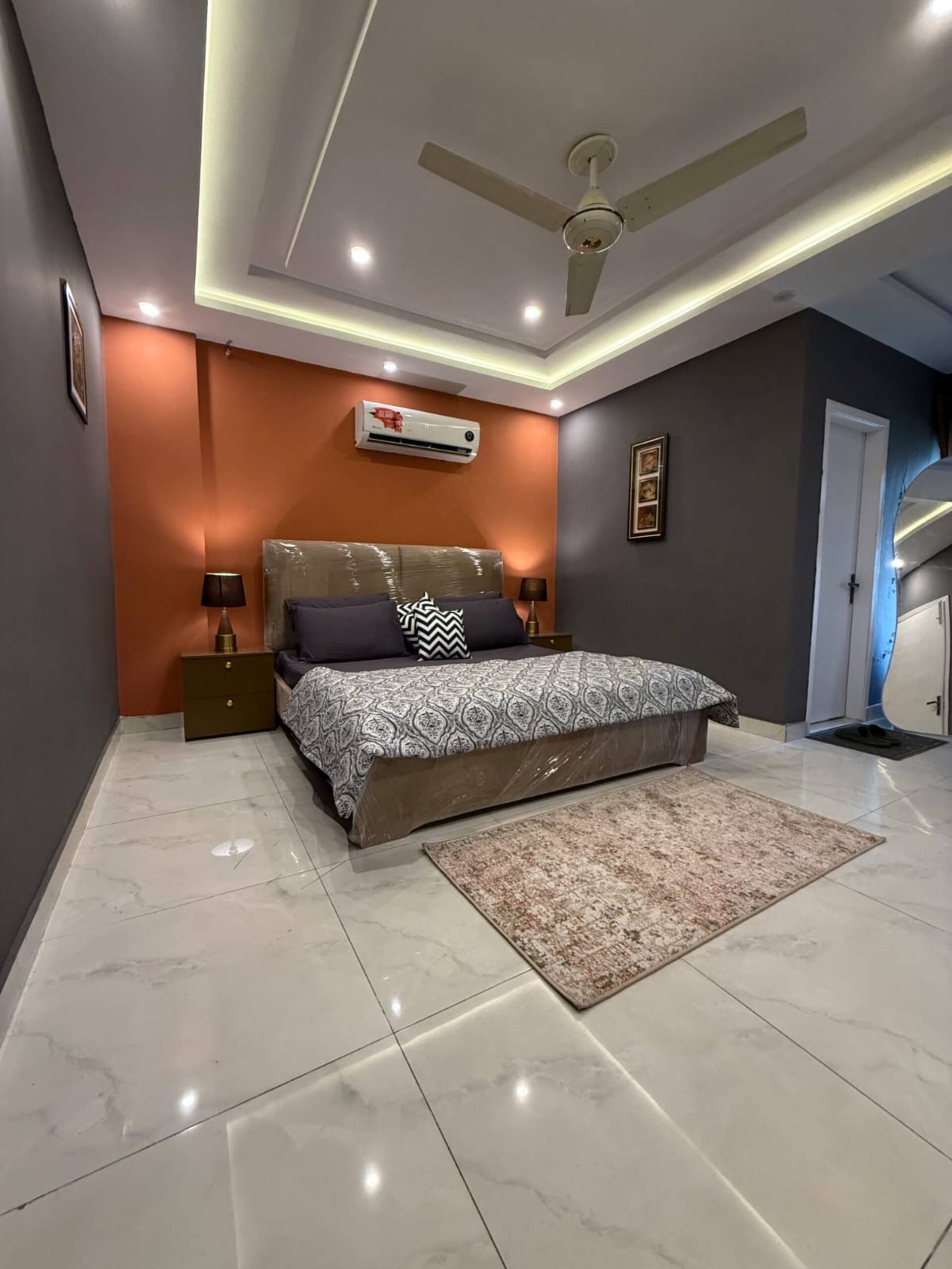 Wide view of the bedroom with king bed, rug and ambient cove lighting in The Amber Haven, the Aangan one-bedroom apartment facing Grand Jamia Mosque in Bahria Town Lahore