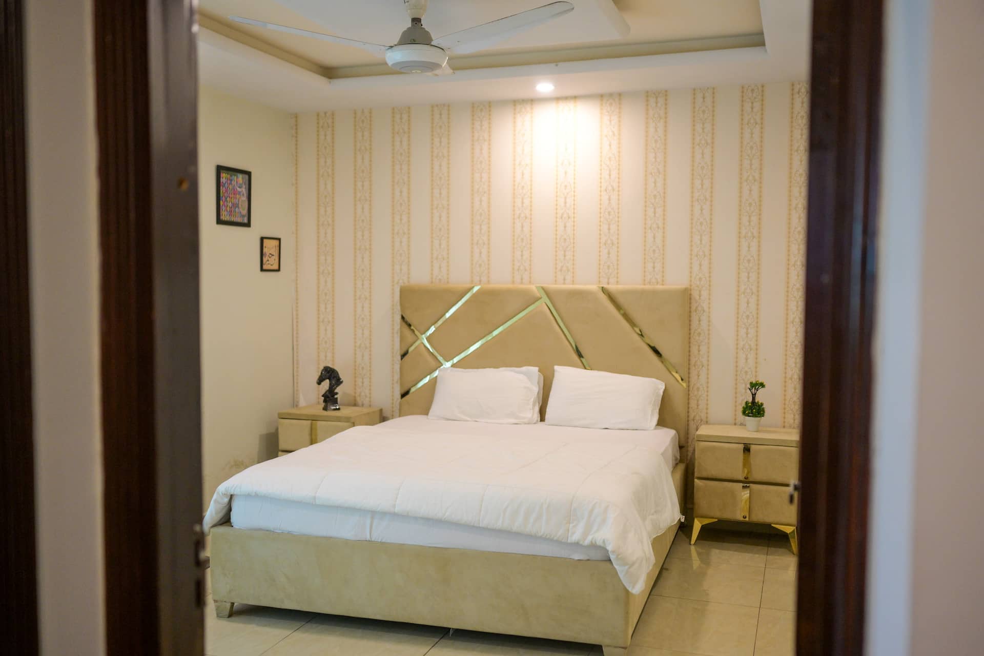 Wide view of a bedroom with a double bed and striped wallpaper in the Aangan three-bedroom gaming suite in Apollo Tower, E-11 Islamabad