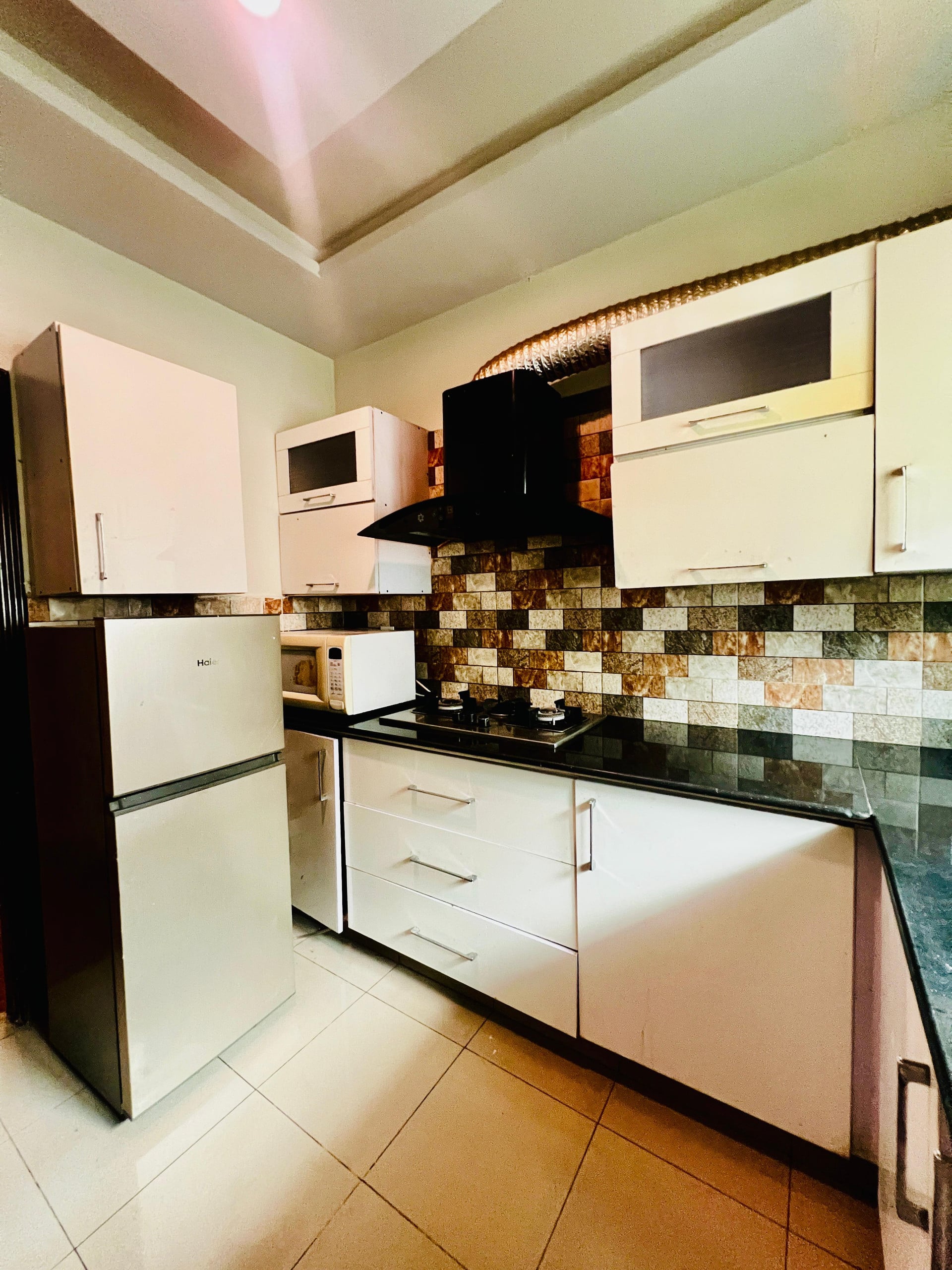 Fitted kitchen with cabinets, refrigerator and tiled splashback in the Aangan three-bedroom gaming suite in Apollo Tower, E-11 Islamabad
