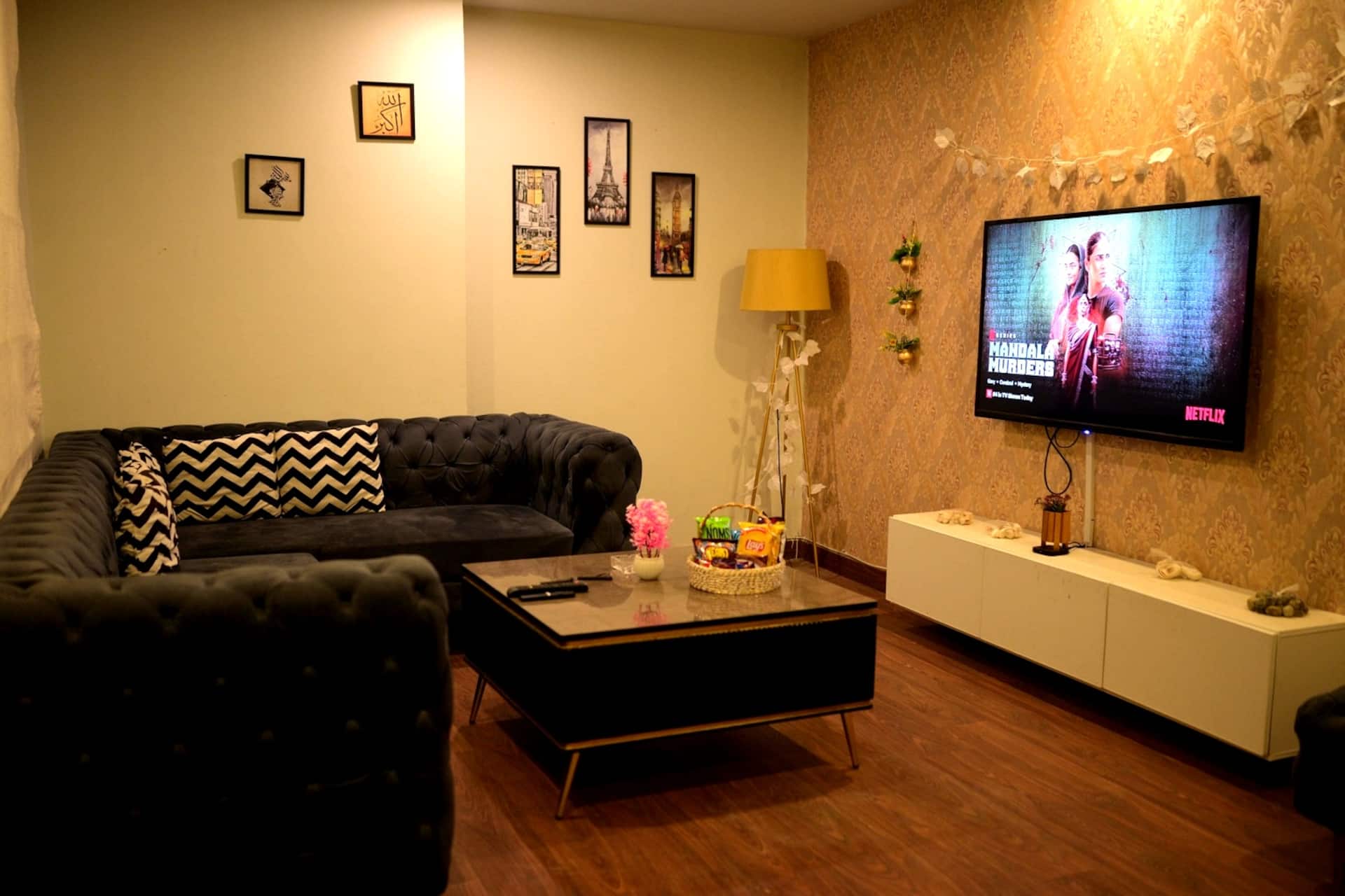 Lounge with a black tufted sofa and wall-mounted TV against a textured wall in the Aangan three-bedroom gaming suite in Apollo Tower, E-11 Islamabad