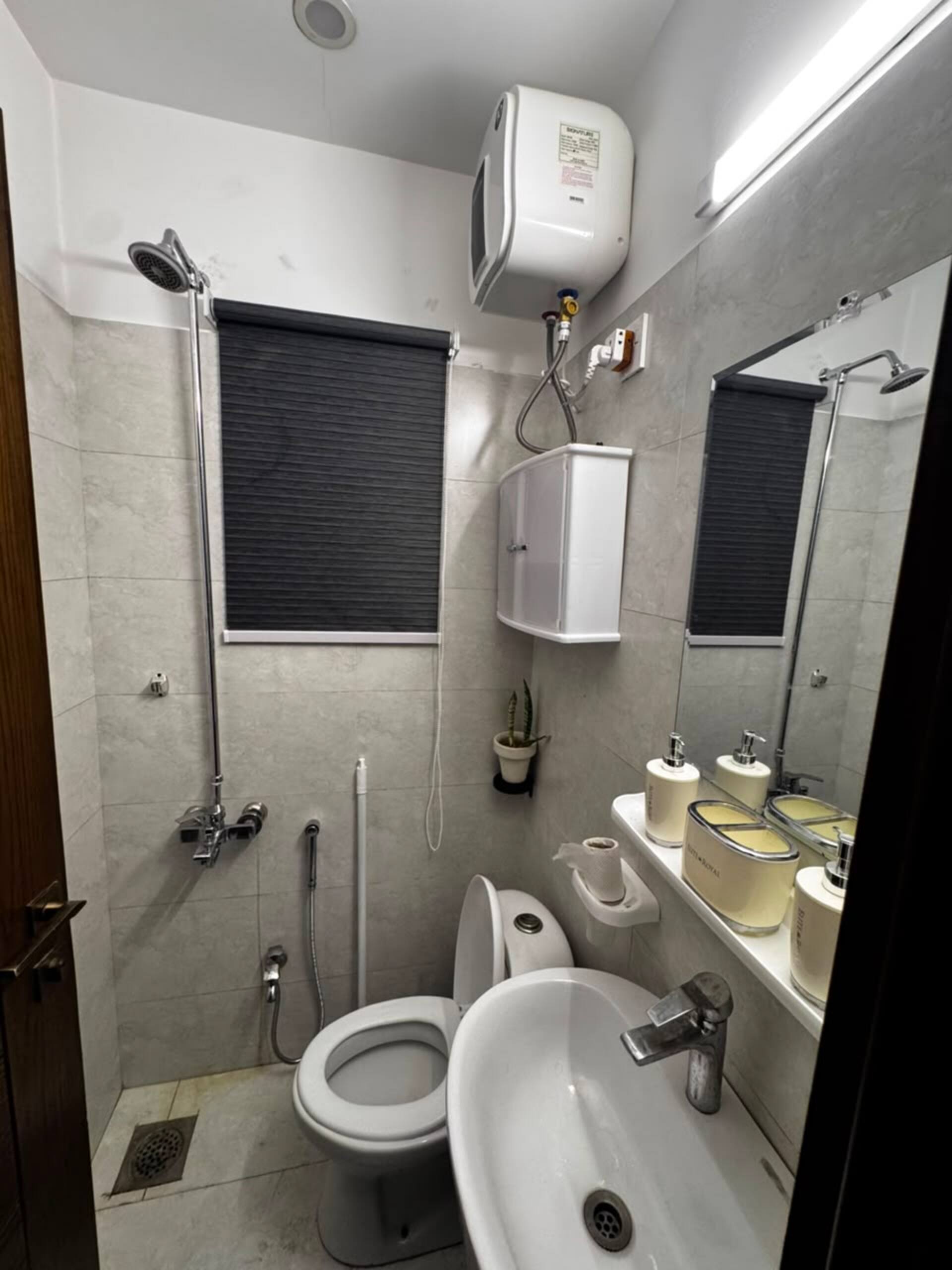 Bathroom with a shower area and water heater in the Aangan studio apartment near Islamabad International Airport
